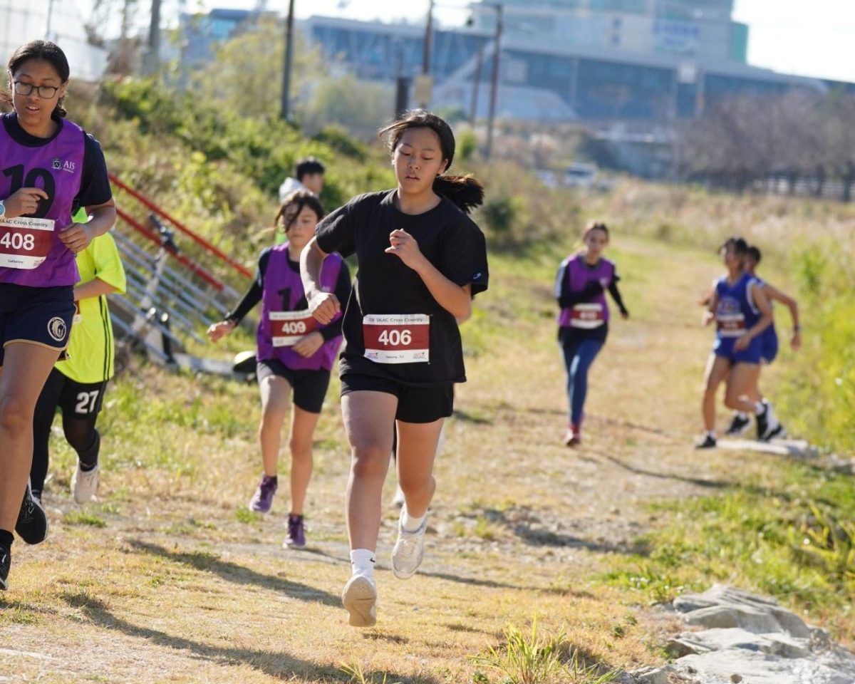 Yul Sakong in 7th grade sprints down the trail, neck and neck with a rival from AIS and closely followed by more competitors.