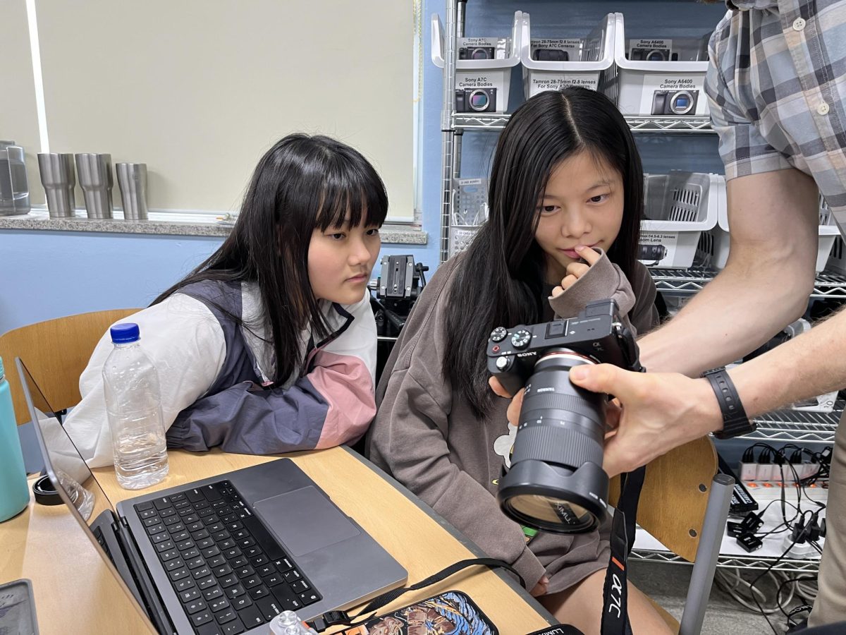 Natsuki Onuma and Peyton Tsai from AAIA watch in amazement while Mr. Lipsky shows them how to work a camera.