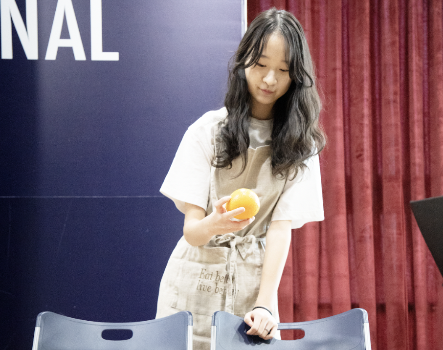 Elena Lee in 8th grade, a farmer alongside Alex Seo, inspects the fresh orange from the basket. She needs to sell them to a customer. 