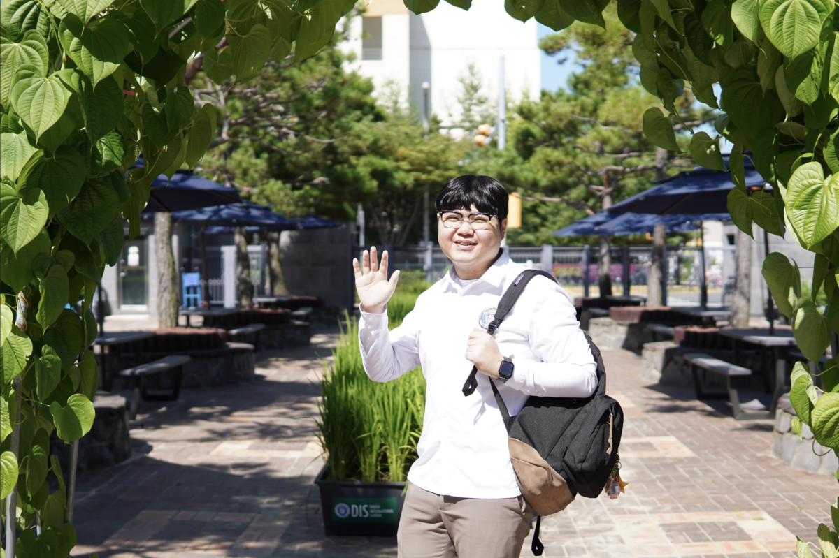 Senior Jackson Chiang waves at the camera as he enters the school through the new greenery of the school. 