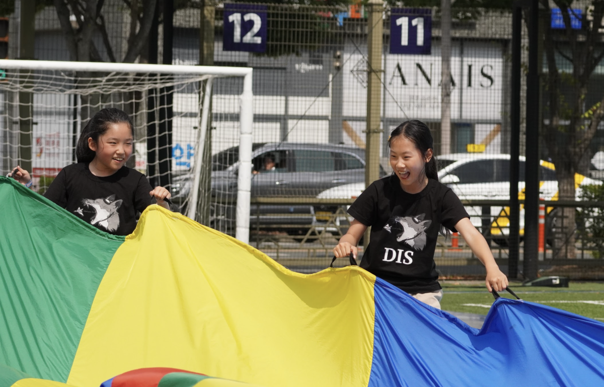 Fourth-graders Maei Jin and Irene Lee expertly maneuver the rainbow parachute. They giggle as their friends lose their grip on the colorful accessory. 