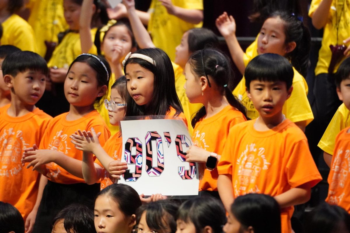 The first, second and third grade assemble on stage to perform songs from the '90s. 