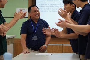 Mr. Hortezuela beams with pride as his physics class erupts in applause, astonished by his quick mastery of a challenging physics question. Students attentively listen to every part of his explanation of the answer in detail, afraid to miss a single step of it.