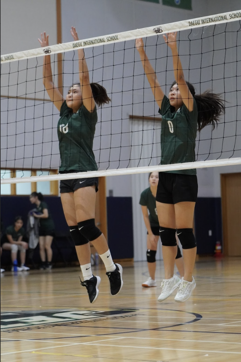 Bonnie Kim (18) and Ellen Cho (0) jump into the air to block a spike. 