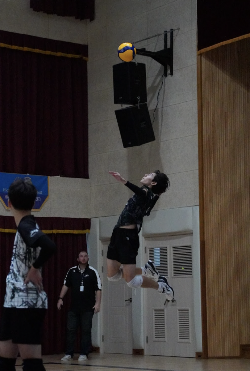 Outside hitter Ethan Rossmeisl (number 5) flies for a top-spin jump serve. It spins into the court, landing in between two defenders. 