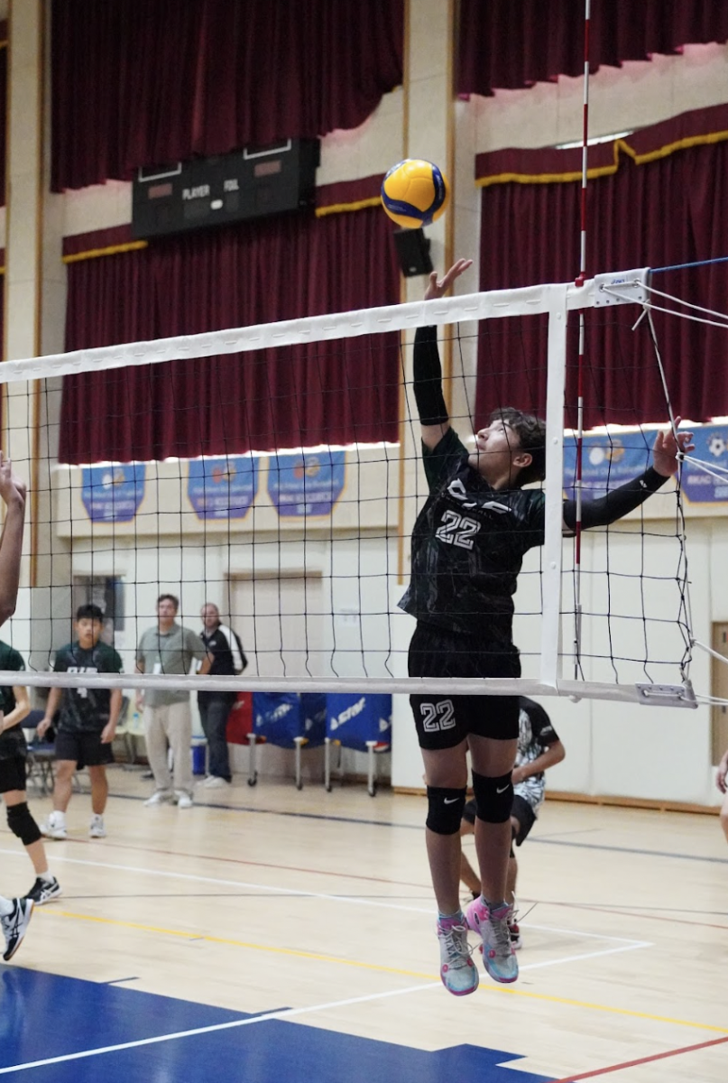 Outside Hitter Noah Don (number 22) tips the ball over the net. Hitting the blockers' hands, it goes out of bounds, earning them a point for the set win.