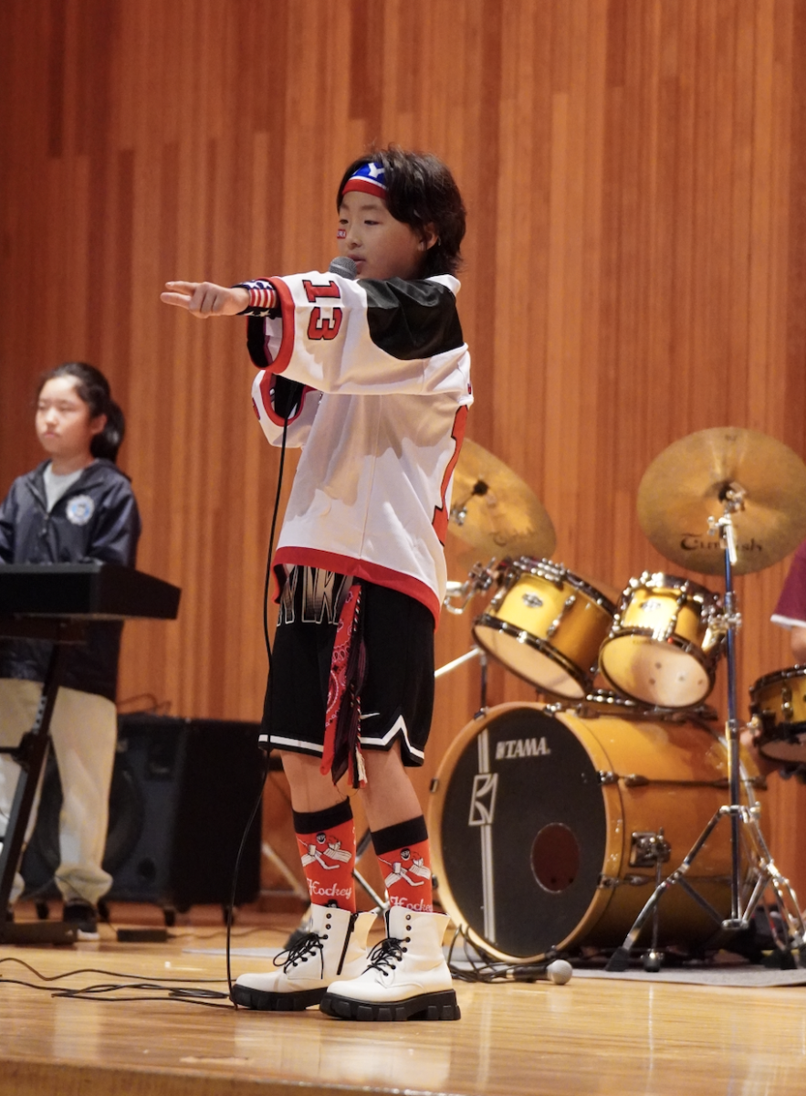 Jason Lee in third grade gestures to the crowd to join in with the music in his stunning outfit. His ability to energize the crowd hints at exciting performances to come. 