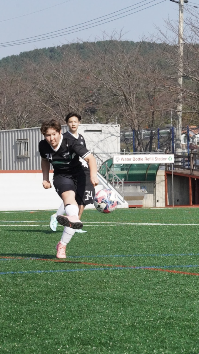 Aiden Hwang (number 34) in sixth grade aims the ball toward the goal with precision and power. He maintains his unwavering focus as he drives toward the goal. 