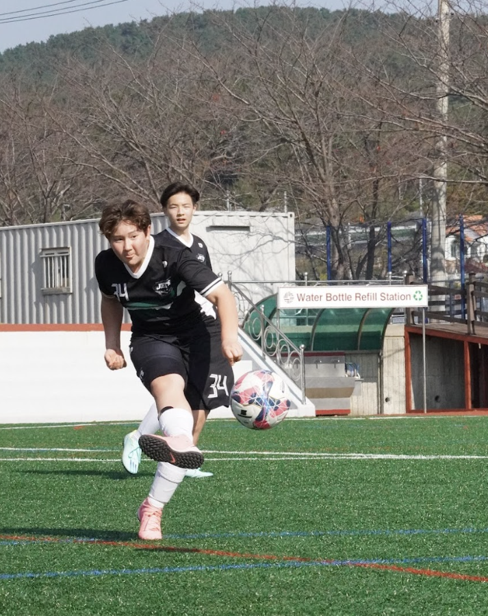 Aiden Hwang (number 34) in sixth grade aims the ball toward the goal with precision and power. He maintains his unwavering focus as he drives toward the goal. 