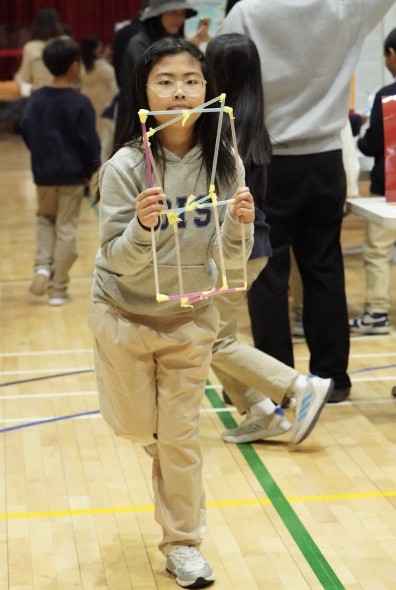 Ruby Kim in third grade carefully embraces her straw tower, reflecting her hard work.