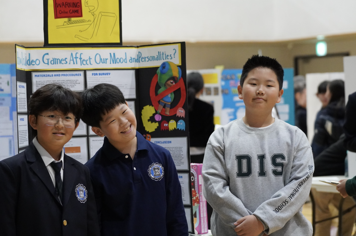 Fifth graders Logan Nam, David Hur, and Brayden Kim proudly showcase their project on the effects of video games on mood and personality. They aim to shine with a first place in their final year of elementary school. 