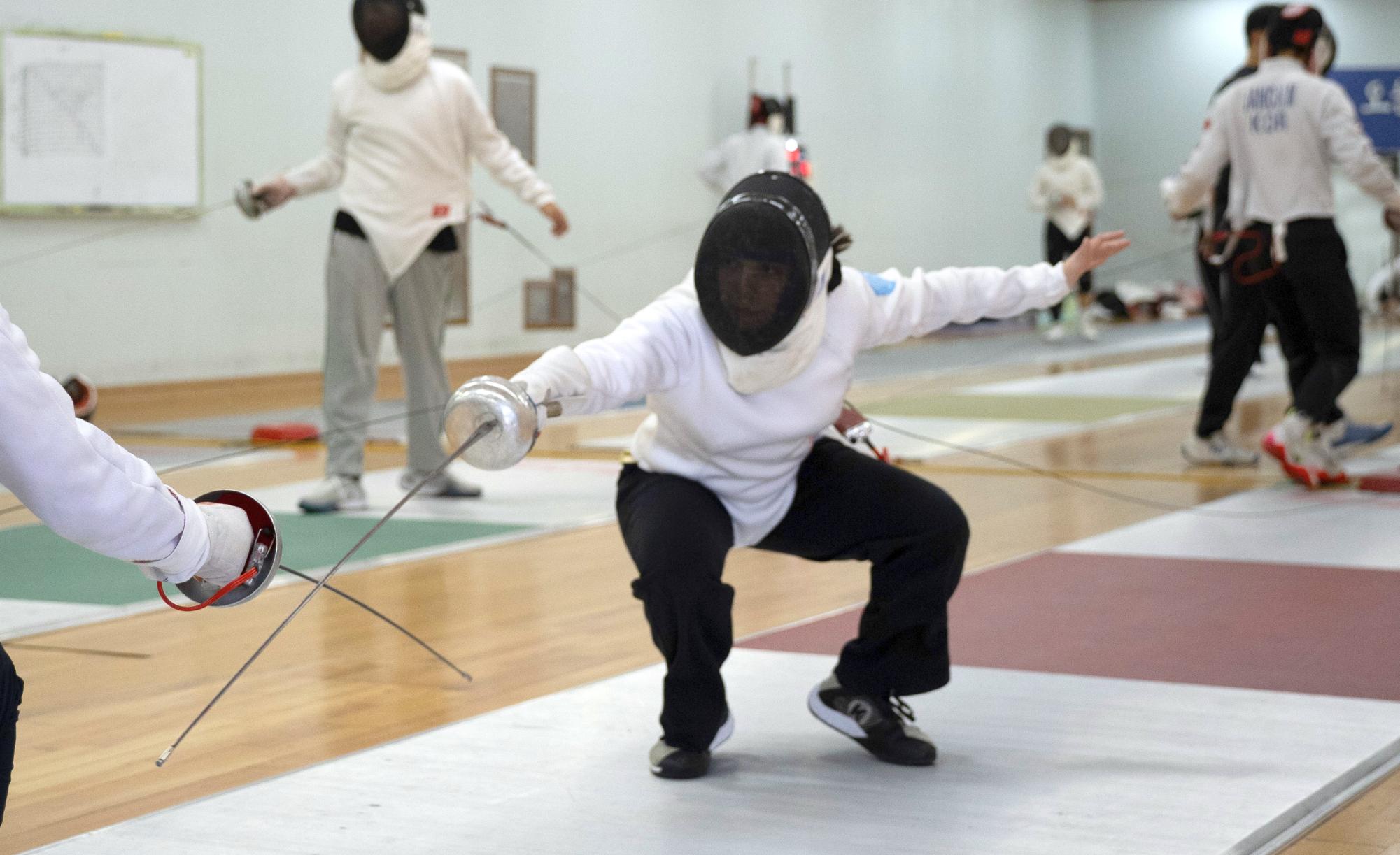 Azul Rivera crouches low as she breaks through the guard of her opponent. With a thrust of brilliance, she earns the point. Coach Lee gives her a thumbs-up.