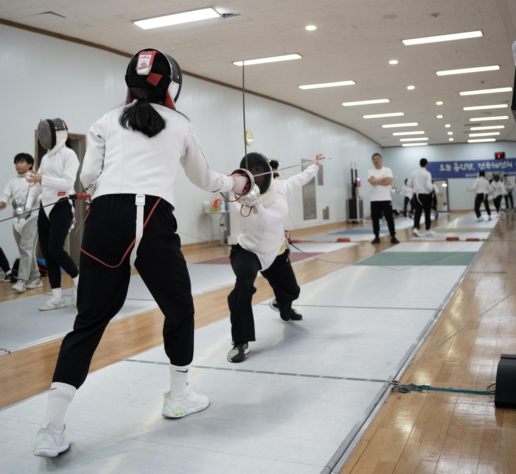 Rivera fends off her opponent's sword and plays the defense. Coach Lee watches from afar, taking mental note of techniques that Rivera should practice for the coming week.
