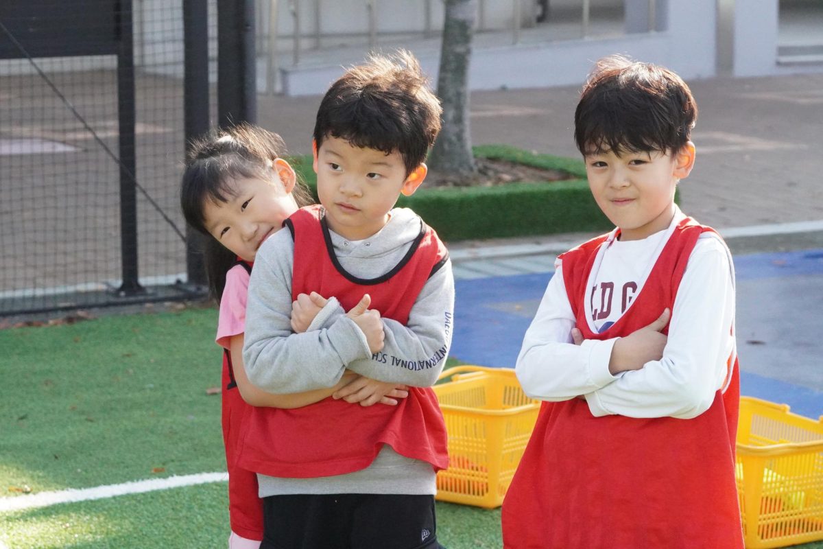 First-graders Brian Hwang, Sienna Woo, and Leo Dzunwien Biern eagerly await the next set of games, their excitement evident as they watch the action unfold. 