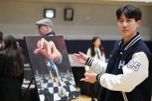 Senior Aaron Shin proudly showcases an artwork created by his peer, Flora Chung. Intricate details and profound thought enliven the exhibit.  