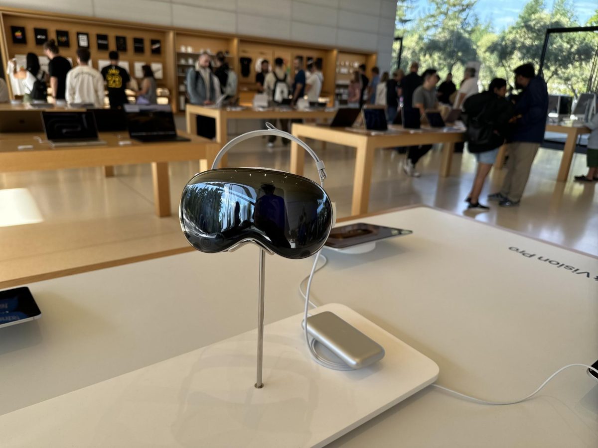 The Apple Vision Pro sits on display at the Apple Park Visitor Center, drawing in tech enthusiasts eager to experience its cutting-edge features. Customers in the background explore Apple's latest innovations, anticipating the future of spatial computing.