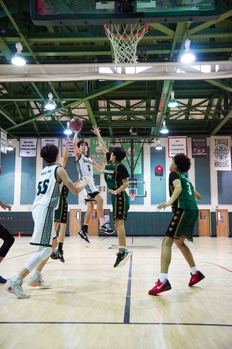 Senior Ethan Rossmeisl (number 5) leaps against a double team. With limited space, he uses one hand to aim for the bucket. After hitting the rim several times, the ball finally drops into the hoop. 
