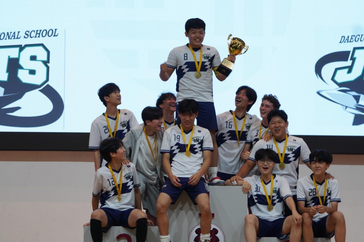 The JV team laughs in triumph on top of the podium, celebrating their win. Despite a freshman-based squad, juniors William Seok (number 8) and Robert Cho (number 18) led them to victory through leadership. 
