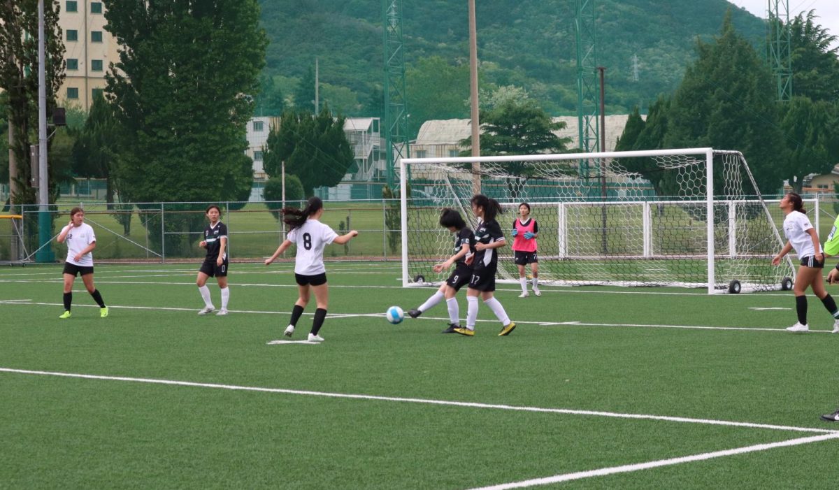 Junior centerback Minori Kojima (9) attempts a quick pass to Sarah, working to clear the ball under pressure. The defense stays alert as they try to regain control and reset the play. 