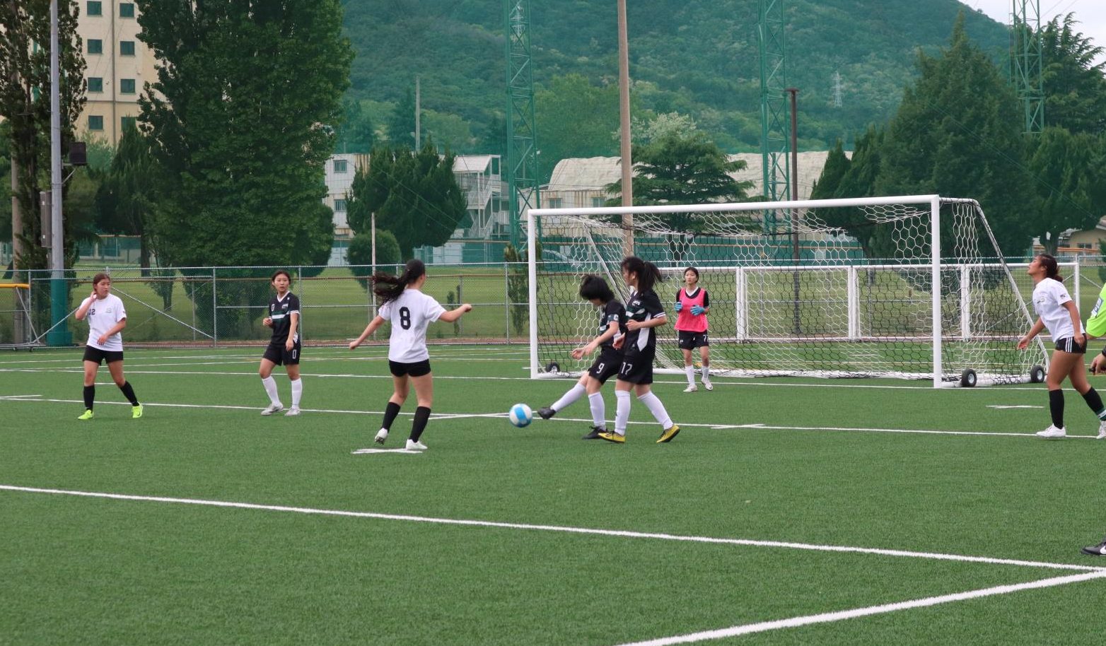 Junior center midfielder Minori Kojima (9) attempts a quick pass to Sarah, working to clear the ball under pressure. The defense stays alert as they try to regain control and reset the play. 