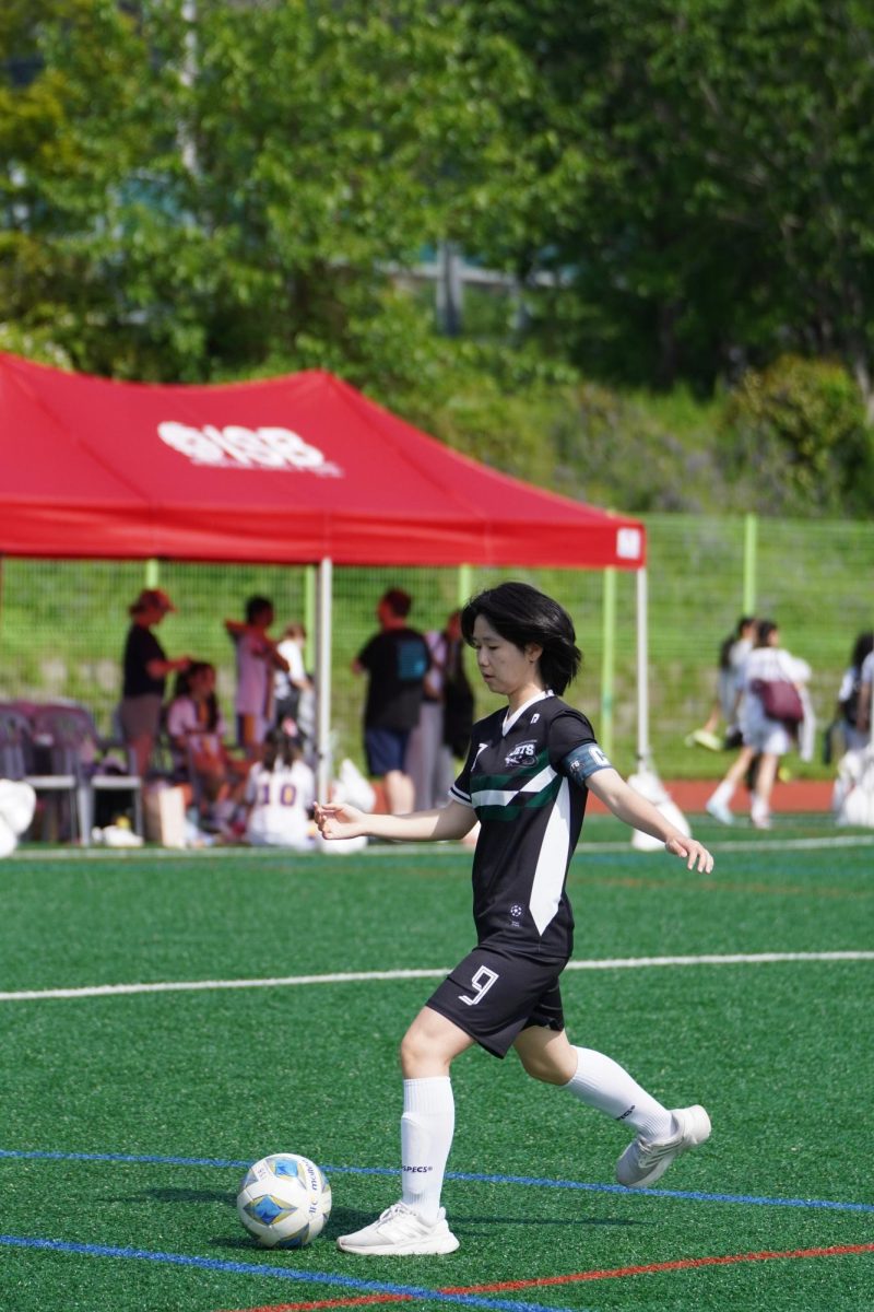 Varsity girls' team captain Minori Kojima (number 9), despite her injuries, holds off ISB's attackers and dishes passes to her teammates as a midfielder. Photo by Tamara Trindade.