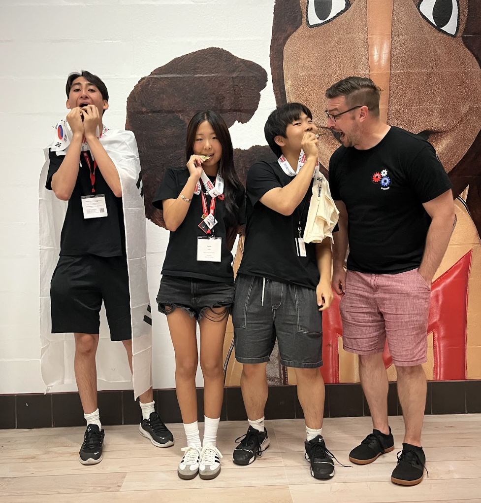 Sophomores Haydn Mangione, Sophie Lee, and Bryan Lee, along with Mr. Kaschub, bite into their gold medals. They take home the top prize, marking a historic first for both DIS and NHD Korea.