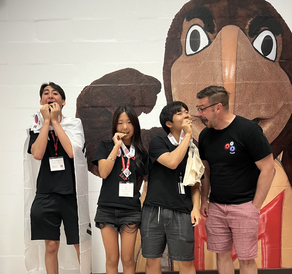 Sophomores Haydn Mangione, Sophie Lee, and Bryan Lee, along with Mr. Kaschub, bite into their gold medals. They take home the top prize, marking a historic first for both DIS and NHD Korea.