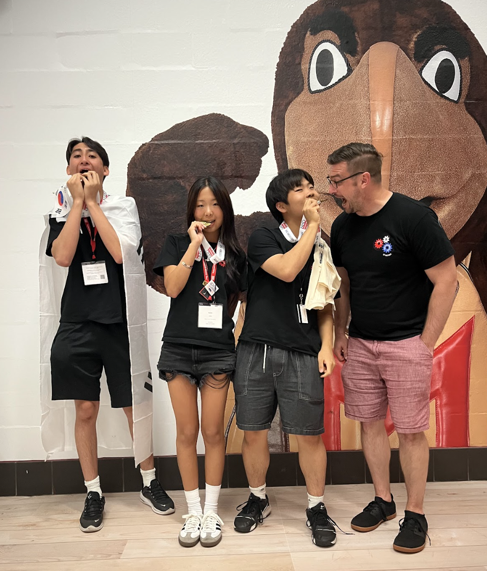Sophomores Haydn Mangione, Sophie Lee, and Bryan Lee, along with Mr. Kaschub, bite into their gold medals. They take home the top prize, marking a historic first for both DIS and NHD Korea.