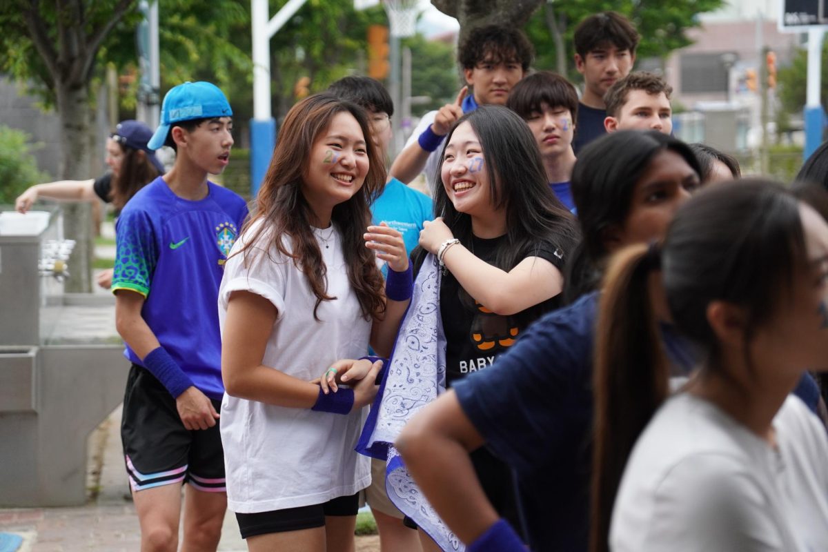 Tenth graders Bonnie Kim and Reina Li share a laugh before the start of Field Day. Excitement and anticipation fill the air as they get ready for the events ahead. 