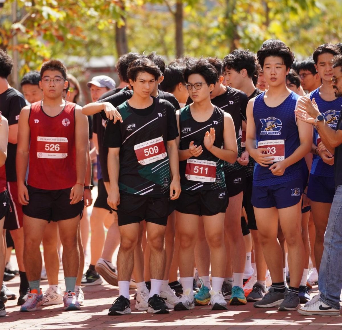 The high school boys line up at the starting line, steadying their breath as anticipation builds. When the whistle blows, they launch forward, ready to conquer the course. 
