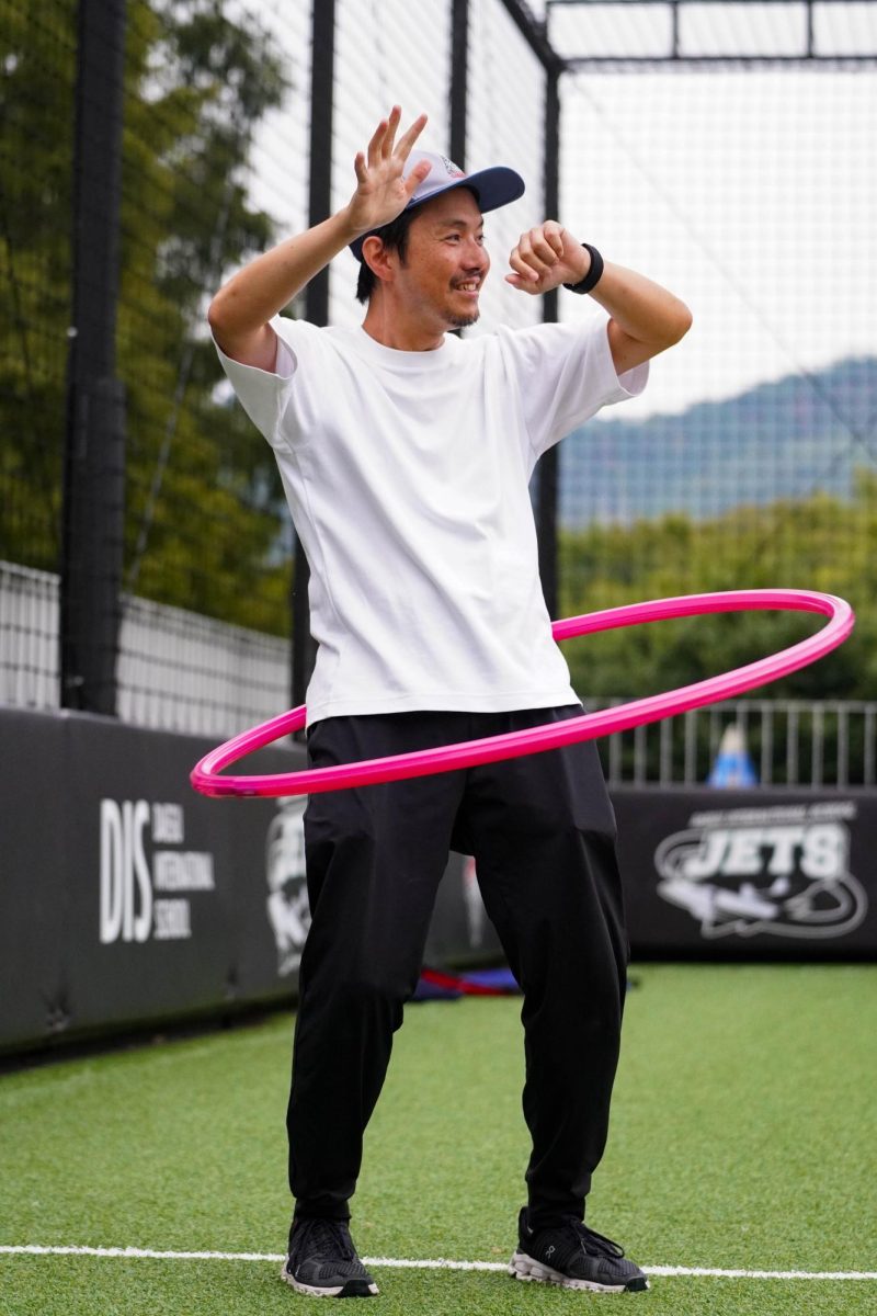 Second-grader Shu Koizumi’s dad sways his hips in determination to keep the hula hoop from falling down. His cheerful laugh and expressive motions bring up the energy of the event. 