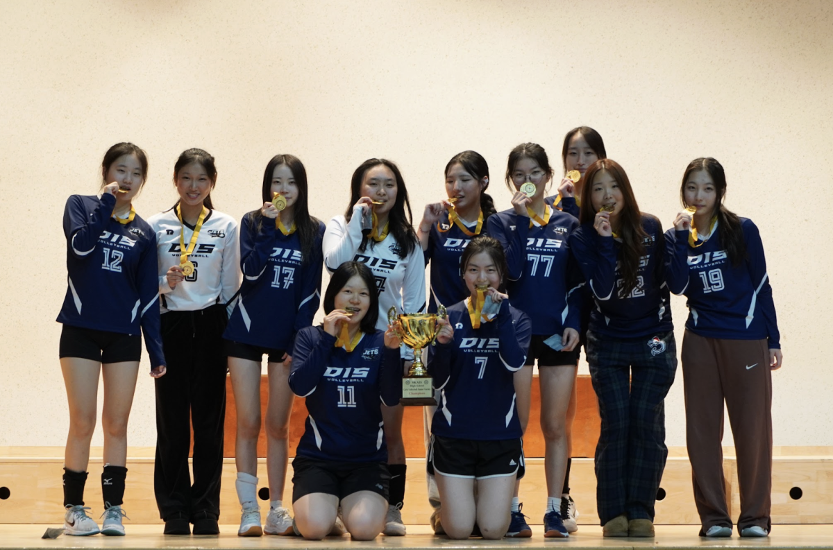 The junior varsity girls bite down on their gold medal for the first time in DIS history. Senior captains Apple Jun (7) and Sophia Bae (11) excitedly hold up their SKAIS championship trophy to celebrate their win. 