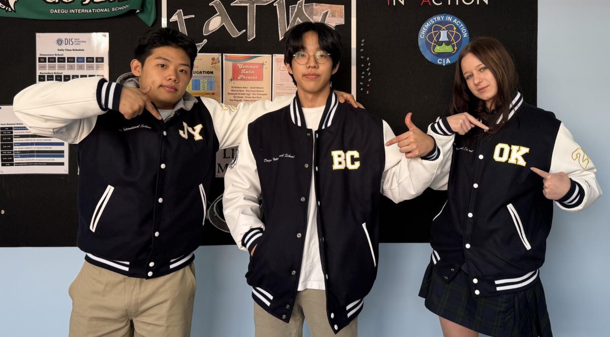 Seniors William Seok, Brian Cho, and Olga Karpenko point to the yellow-stitched initials on their jackets. The Class of 2026 personalized their coats by choosing their own initials to make each one unique.