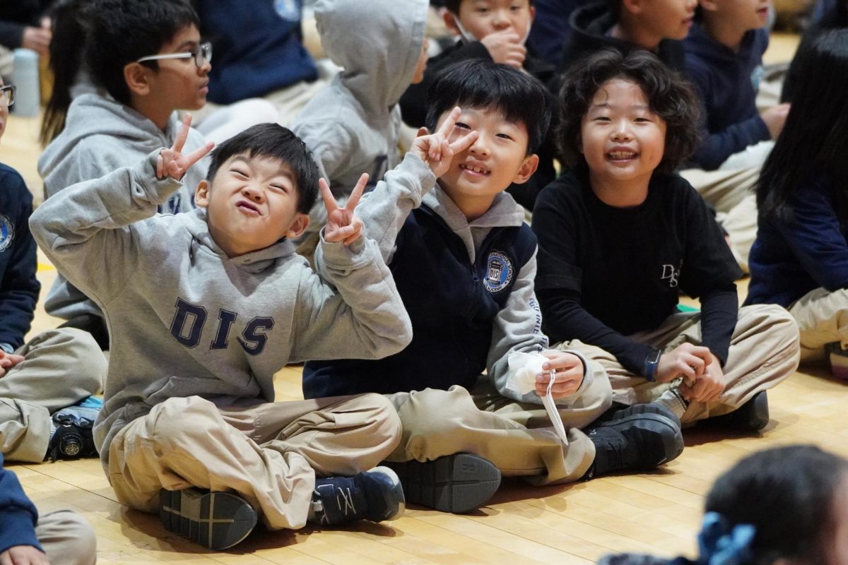 First graders Ryan Cho, Sean Lee and Julian Jung sit together among the assembly crowd. The group stands out as they settle in alongside their peers in matching school uniforms. 