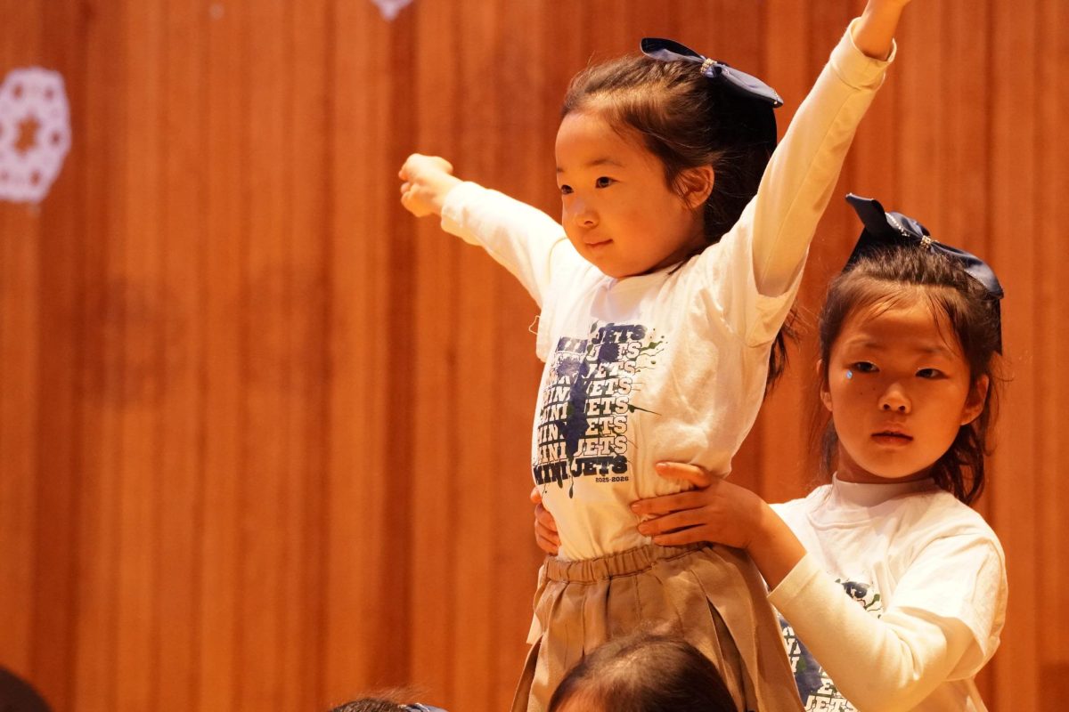 First grader Alice Kim lifts into position as her fellow cheerleaders carry her arms extended and locked in. The cohort carries the move through the routine with steady coordination.