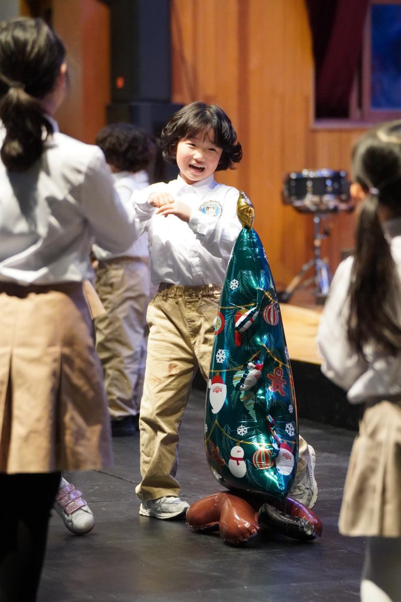 First grader Julian Jung surrounds the balloon tree with his peers. Amusing performances and festive decorations allow him to celebrate his second Winter Fine Arts Festival with joy.