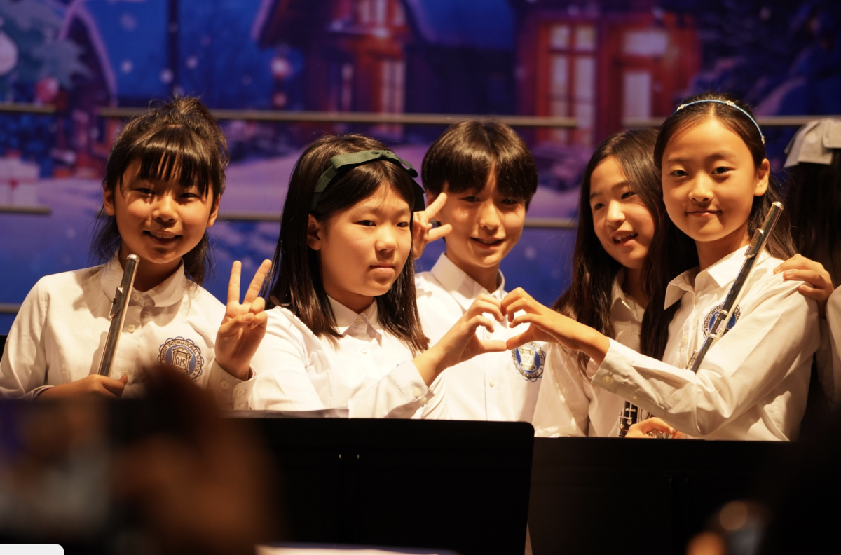 Fifth graders gather on stage during the performance, standing shoulder to shoulder as they share a quiet moment before the music continues. Their close formation reflects the camaraderie and confidence built through rehearsals and ensemble work.
