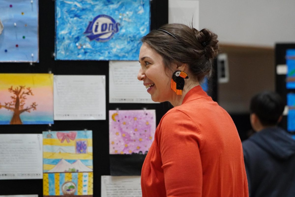 Elementary art teacher Mrs. Gum engages with the elementary art exhibition as she observes the work displayed along the gallery wall. The collection features pieces where students explore artistic aspects from weeks of practice.