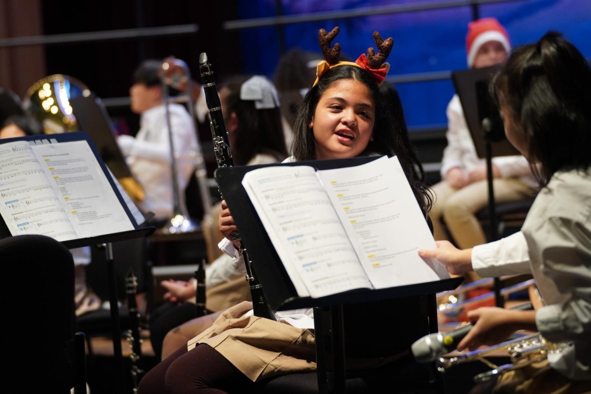 Fifth grader Sofi Akl chats quietly with her peers before they begin their musical piece. To ease nervousnesses, they cheer each other on and build confidence. 