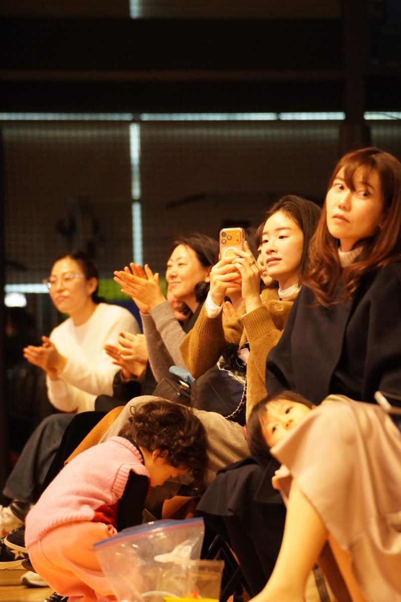A group of parents eagerly capture their children’s performance from the sidelines. The audience watches attentively, reflecting the progress students achieved over the semester. 