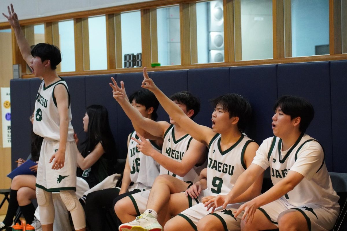 Varsity bench players erupt from the sidelines after a clutch bucket drops, rallying behind their teammates with animated celebrations. Their sideline energy fuels momentum and keeps the intensity high on the court.