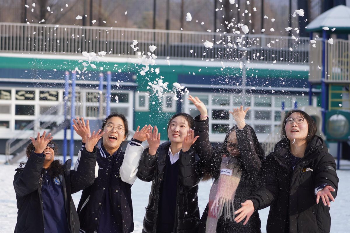 A group of senior girls fling the snow up into the air, letting the soft flakes rain down over them. The girls tilt their head back trying to catch the drifting power.  