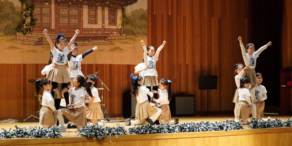 The Mini Jets form a formation with powerful poses, their arms raised with pom-poms in hand. Their coordinated movements and expressions reflect their teamwork, creativity and passion. 