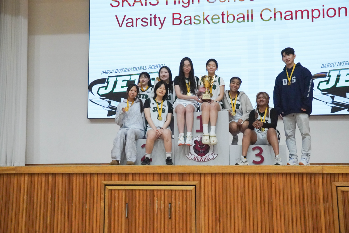 The JV girls’ basketball team celebrates their championship victory for the first time in years. The group gathers with medals and the trophy, ending the season on a high note. 