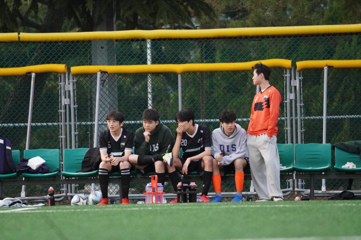 The bench players lean forward, tracking each and every play as the match unfolds on the field. Their focused expressions and sideline communications build intensity for the match as they ready themselves to step in. 