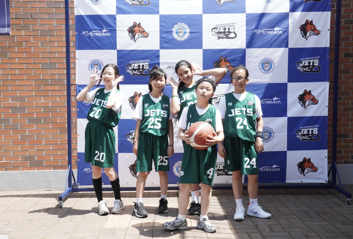 After a competitive weekend filled with strong play and teamwork, the DIS girls gather in front of the DIS backdrop to celebrate their effort and growth. As the tournament comes to a close, the team finishes on a high note together. 