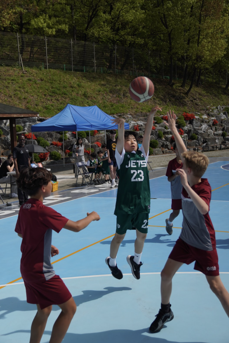 Third grader Ben Lee drives into open space and pulls up for a mid-range jumper over two defenders. With quick movements, he releases the shot as the defense closes in for a block. 