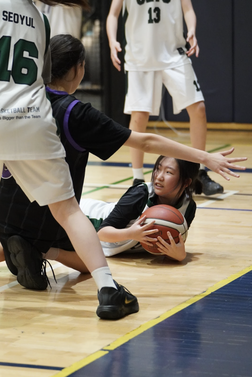 Sophia Sung (0) secures a loose ball while on the floor as her opponents converge around her. Sung’s hustle preserves possession for the Jets and prevents a potential turnover during a crucial sequence of play.