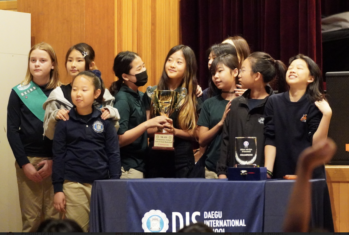 The girls’ basketball team rushes forward to accept the championship trophy. The moment celebrates the hard work and dedication that led to the victory.