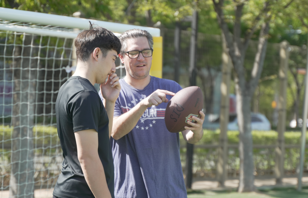 Advisor Dr. Willette coaches junior Noah Hwang on how to lace his fingers around a football.